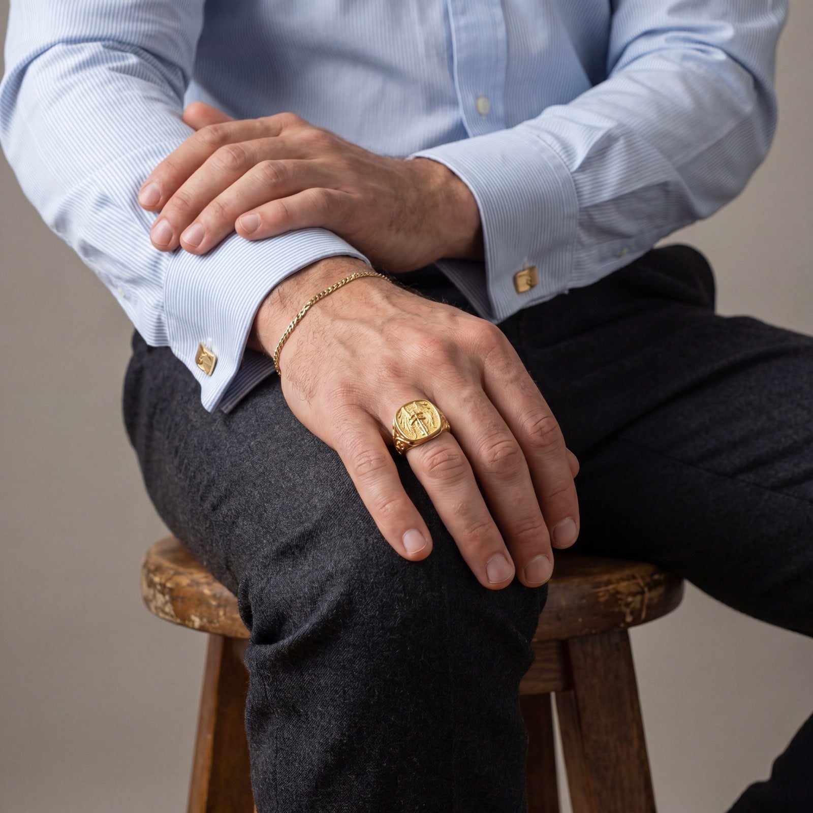 Man wearing the 18k gold Saint Michael signet ring, seated in a French-cuff shirt, hands at rest